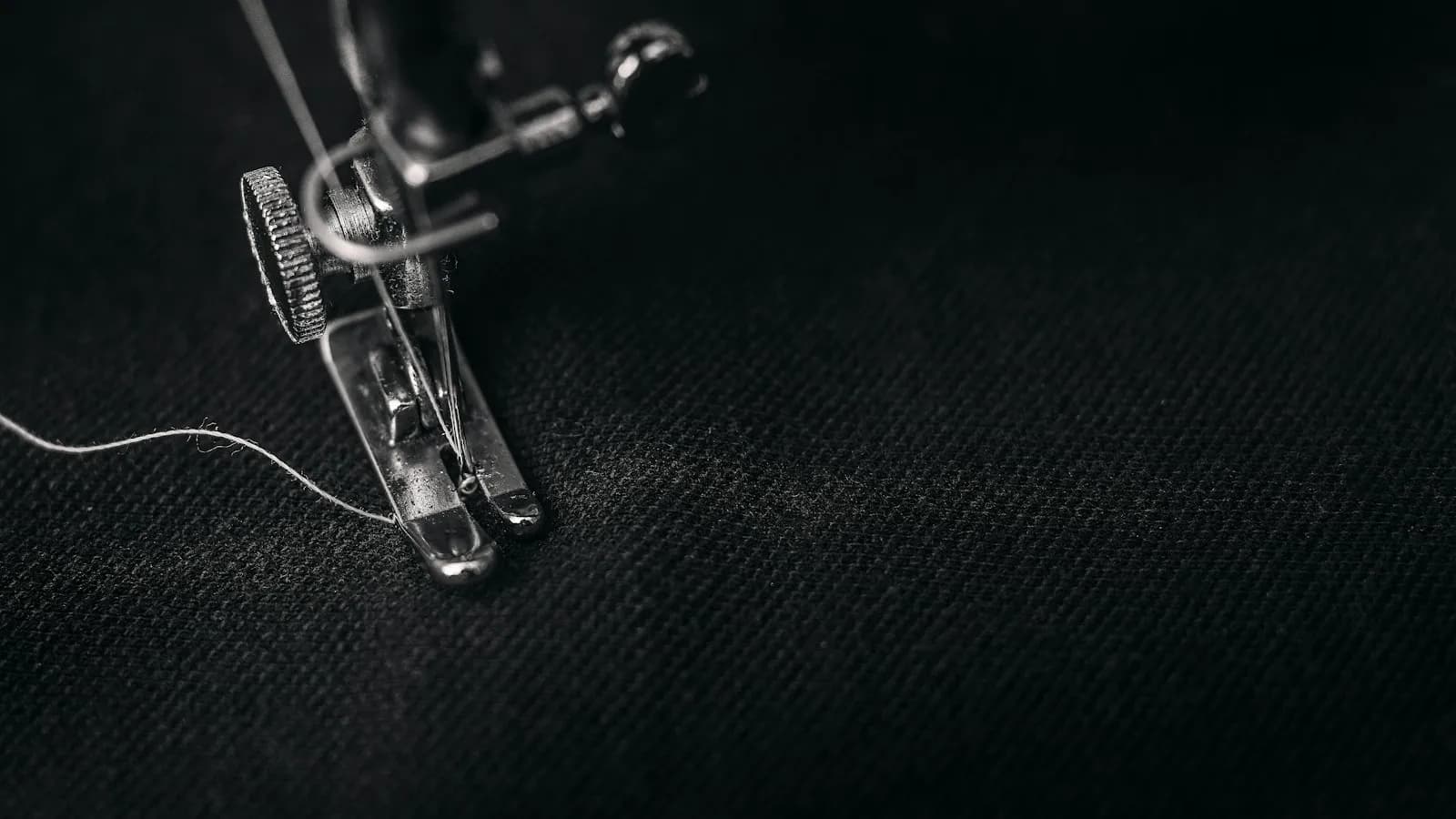 Pied presseur d'une machine à broder en chrome sur tissu noir, fil tendu, ambiance macro.