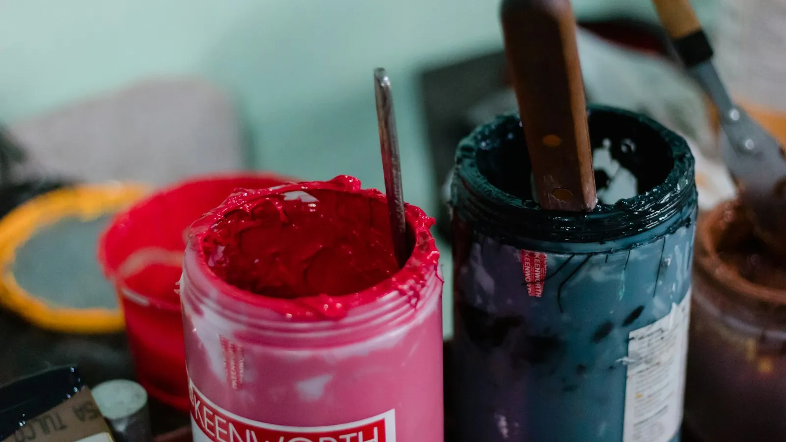 Pots d'encre de sérigraphie, rouge vif et bleu nuit, avec spatules en bois plantées dedans.