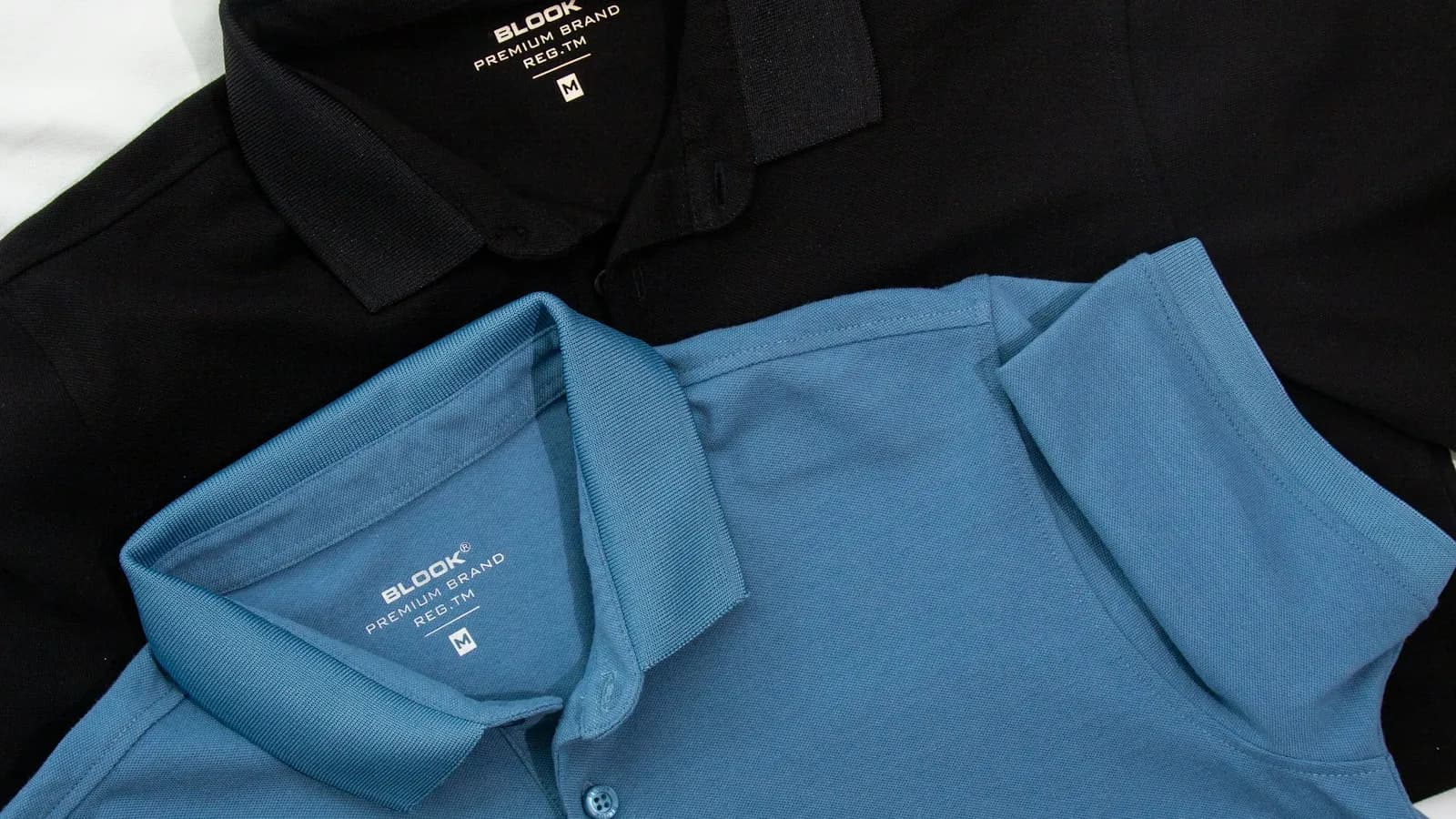 Trois polos premium superposés — blanc, noir, bleu — avec marquage typographique sobre.