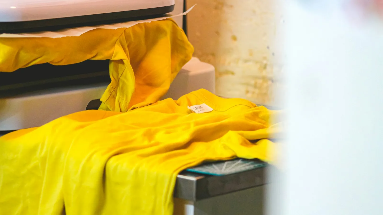 T-shirt jaune posé sur le plateau d'une presse thermique, prêt pour le thermocollage.